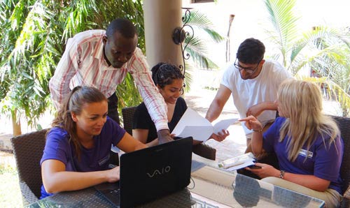 A photograph of volunteer students on a laptop in the company of local workers