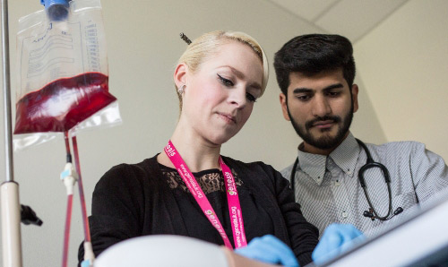 Two people looking down at something next to an IV with blood in it