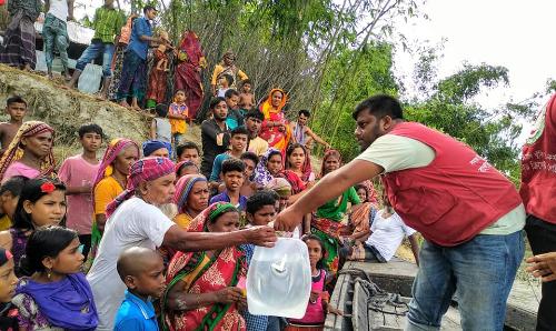 A male aid worker handing water to a crowd of people.