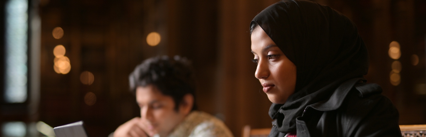 Female student wearing a hijab looking at her laptop.