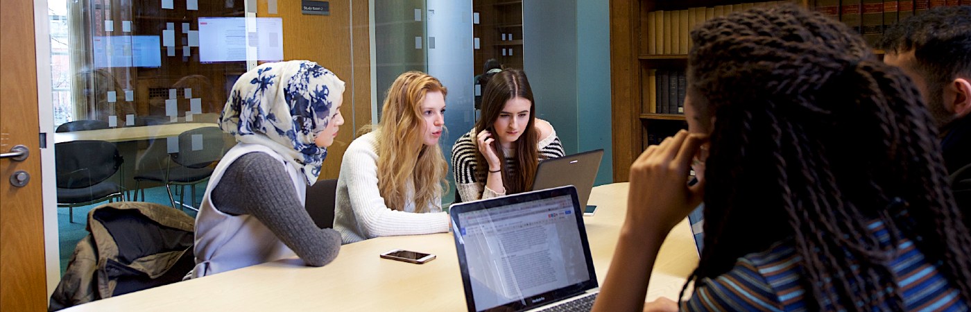 Five students sat around laptops having a conversation.