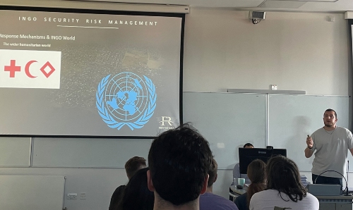 Presenter delivering an INGO security risk management training session, with Red Cross, Red Crescent and United Nations logos projected on screen.